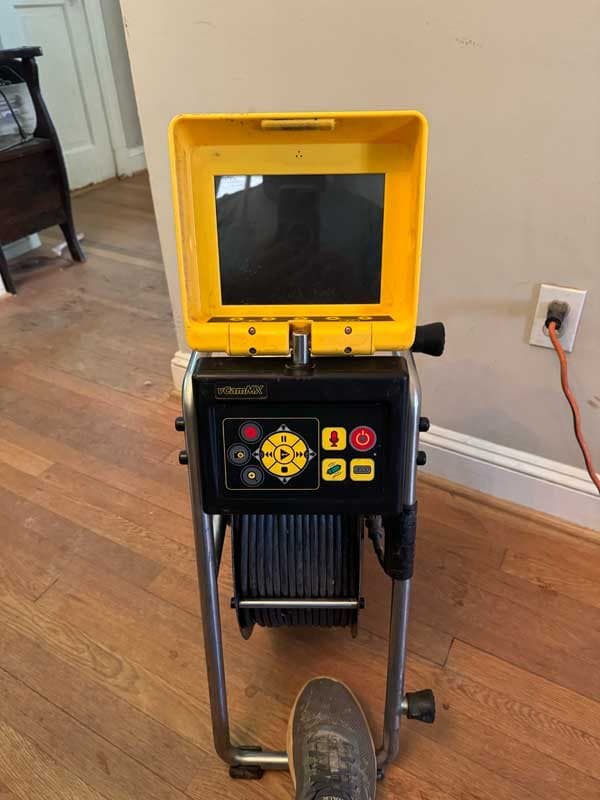 A-1 Trenchless sewer inspection camera monitor with a yellow lid set up on a hardwood floor inside a home