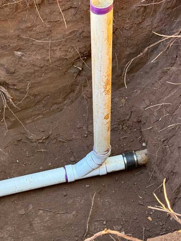 New PVC wye fitting and cleanout riser connected to a sewer lateral at the bottom of an excavation