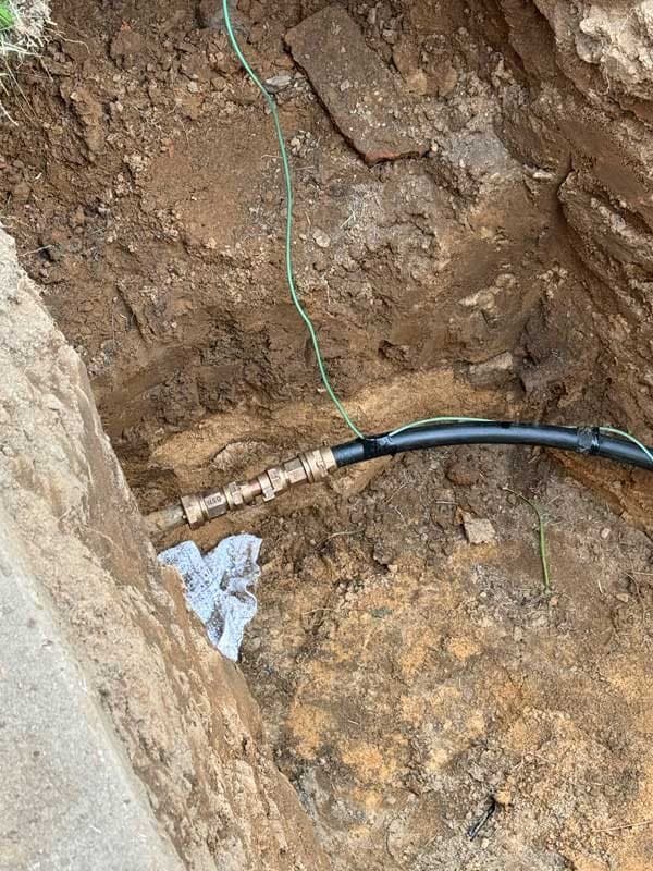 Water service line exposed in a dirt trench, old copper joined to new black water line with a brass compression fitting