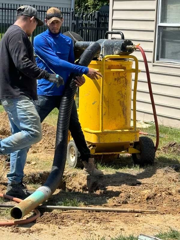 Two A-1 Trenchless crew members beside equipment with a large hose running into a small access pit next to a house